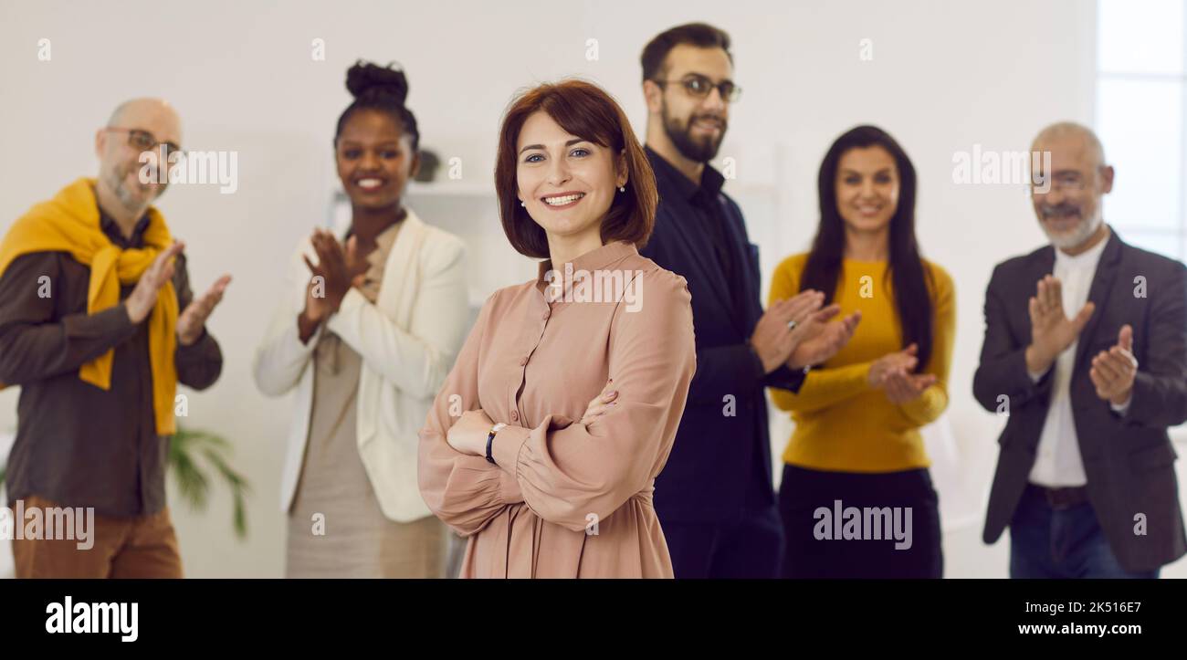 Porträt einer glücklichen Geschäftsführerin mit einem Team von Kollegen, die im Hintergrund applaudieren Stockfoto