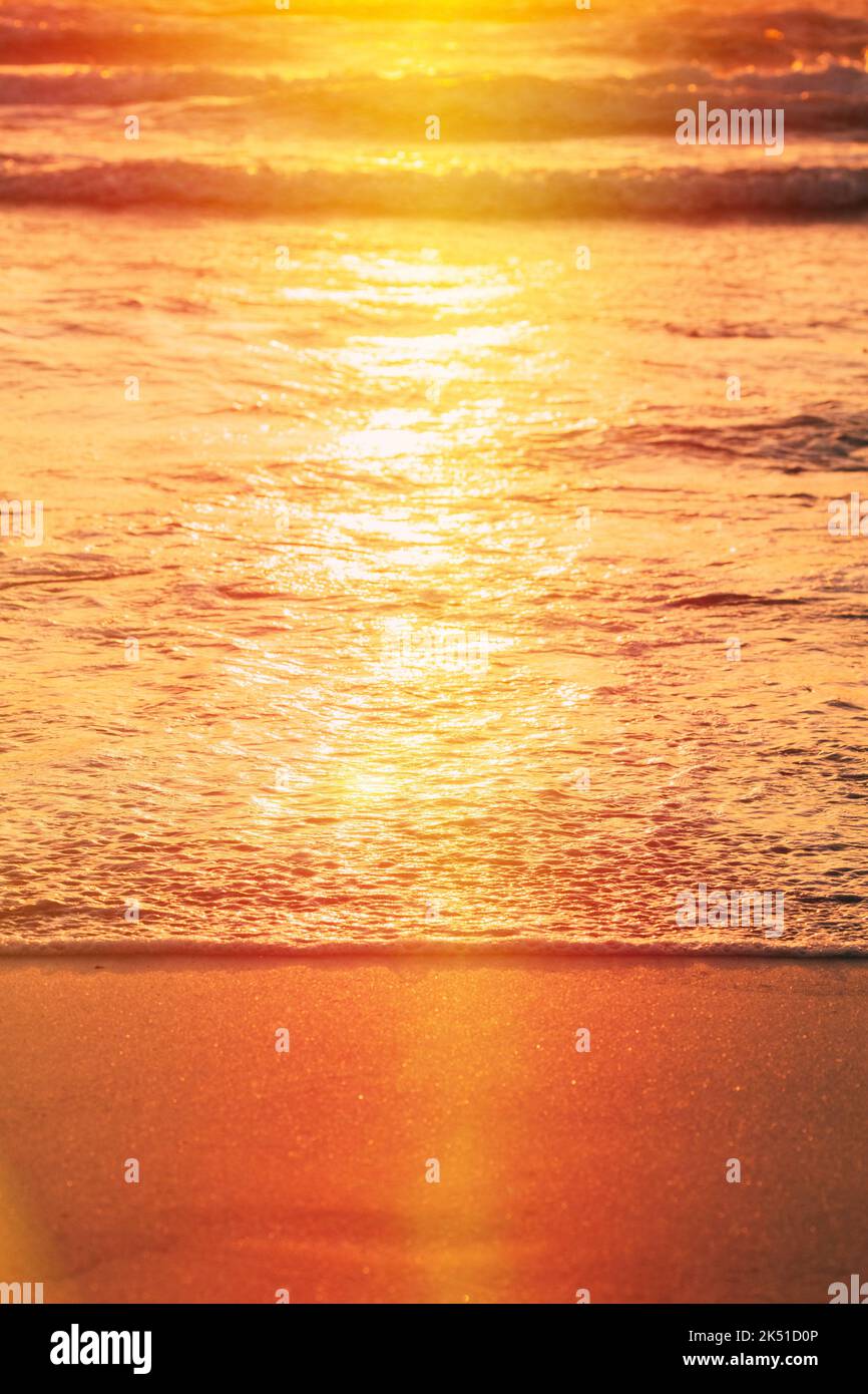 Sonnenuntergang über dem Meer. Riplpe Meer Ozean Wasseroberfläche mit kleinen Wellen. Ozean Wasser Schaum Spritzwasser waschen Sandstrand. Vertikales Foto Stockfoto