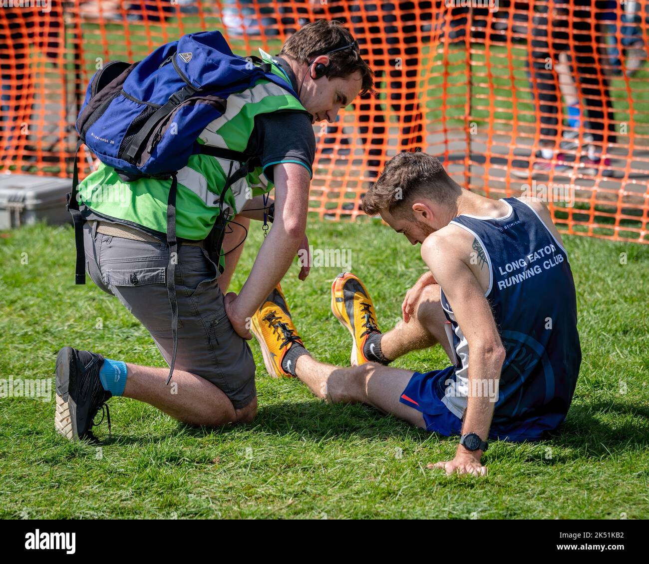 Ein Sanitäter, der am Ende eines Rennens einen männlichen Läufer am Boden besucht. Stockfoto