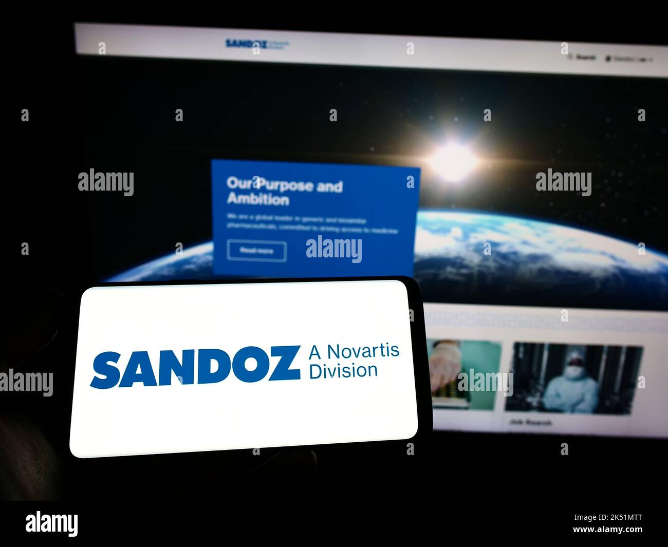 Person, die das Mobiltelefon mit dem Logo des Pharmaunternehmens Sandoz International GmbH auf dem Bildschirm vor der Webseite hält. Konzentrieren Sie sich auf die Telefonanzeige. Stockfoto