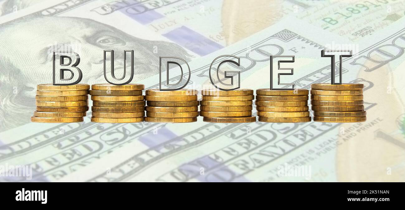 Das Wort 'Budget' besteht aus Glasbuchstaben, die auf Münzstapeln vor dem Hintergrund von Dollarscheinen stehen. Das Konzept eines sauberen Budgets. Stockfoto