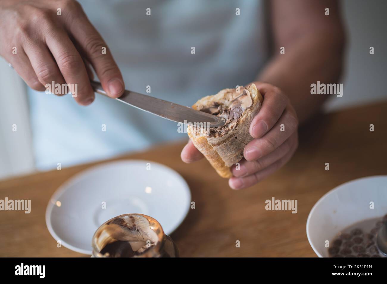 Mann in der Küche beim Frühstück und beim Aufsetzen von Schokoladenpaste auf Brot Stockfoto