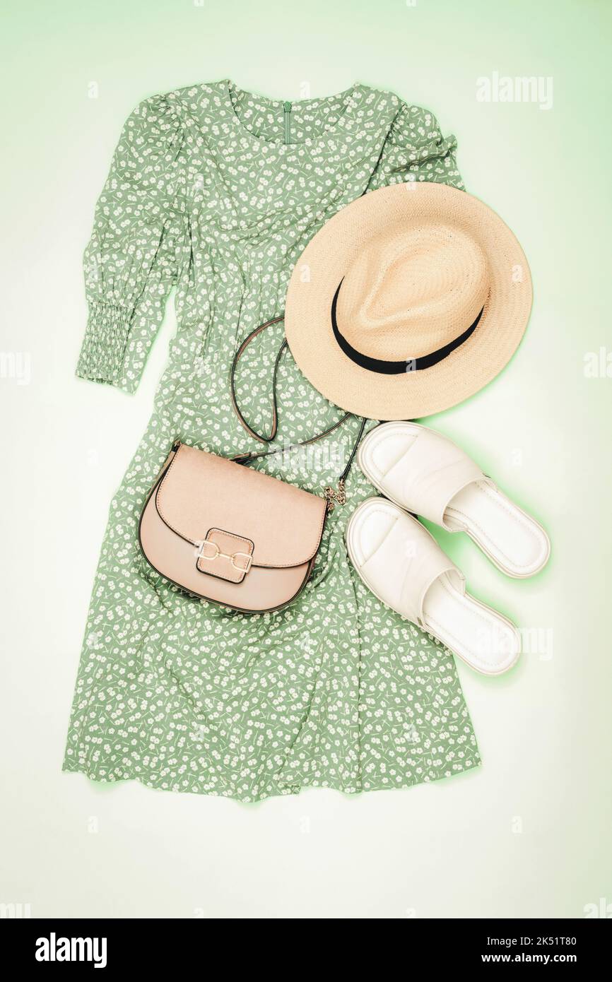 Sommerlicher Casual-Style. Stilvolle Frau Outfit, Kleid, Strohhut, Sandalen und Handtasche auf hellgrünem Hintergrund. Flach liegend, Draufsicht. Stockfoto
