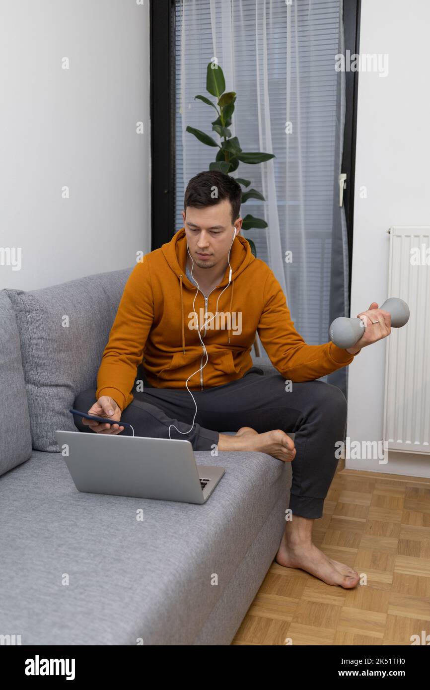 Junger Mann, der zu Hause auf der Couch sitzt und trainiert Stockfoto