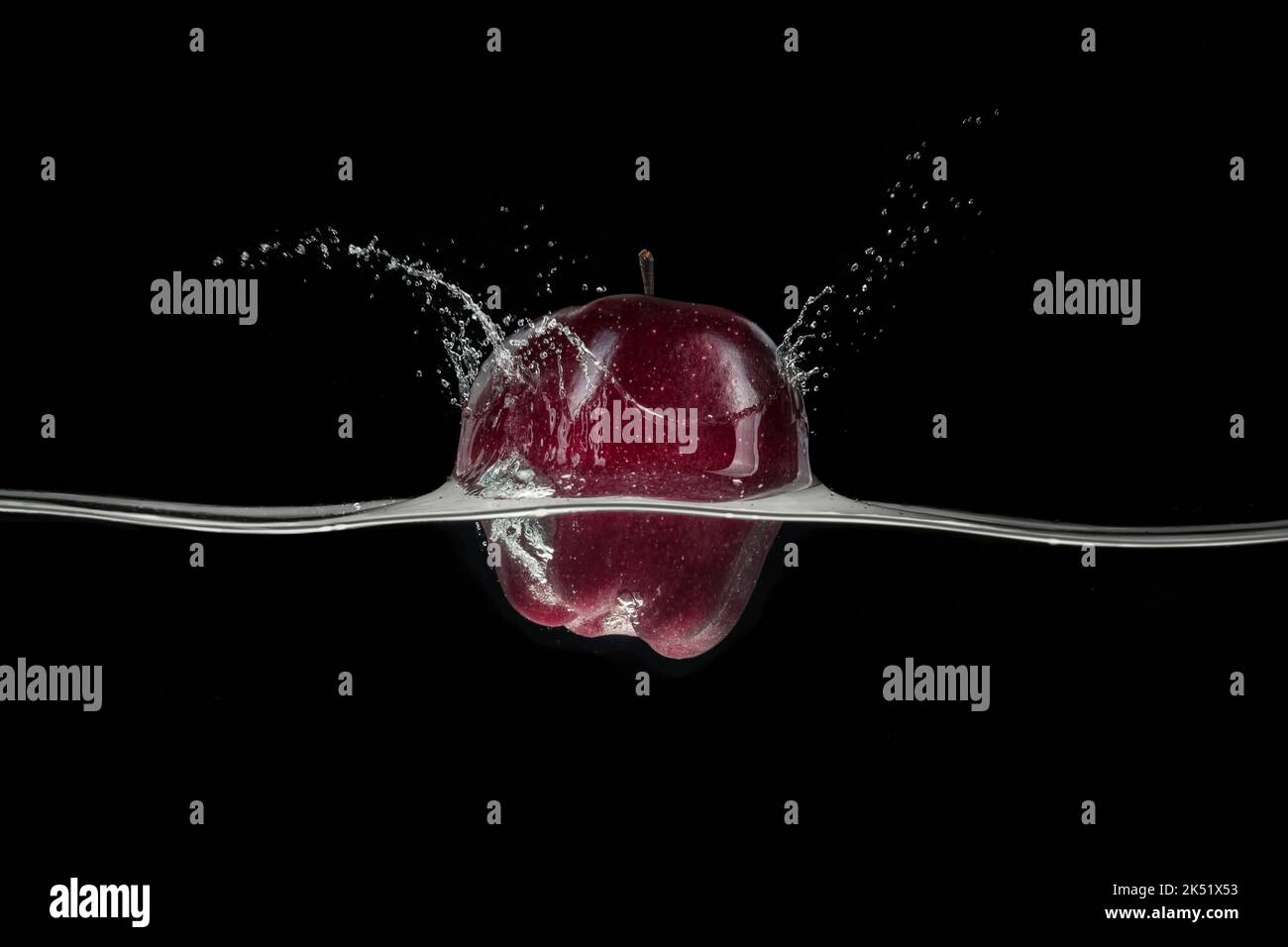 Roter Apfel, der im Wasser spritzt, von einer Seite auf schwarzem Hintergrund betrachtet. Stockfoto