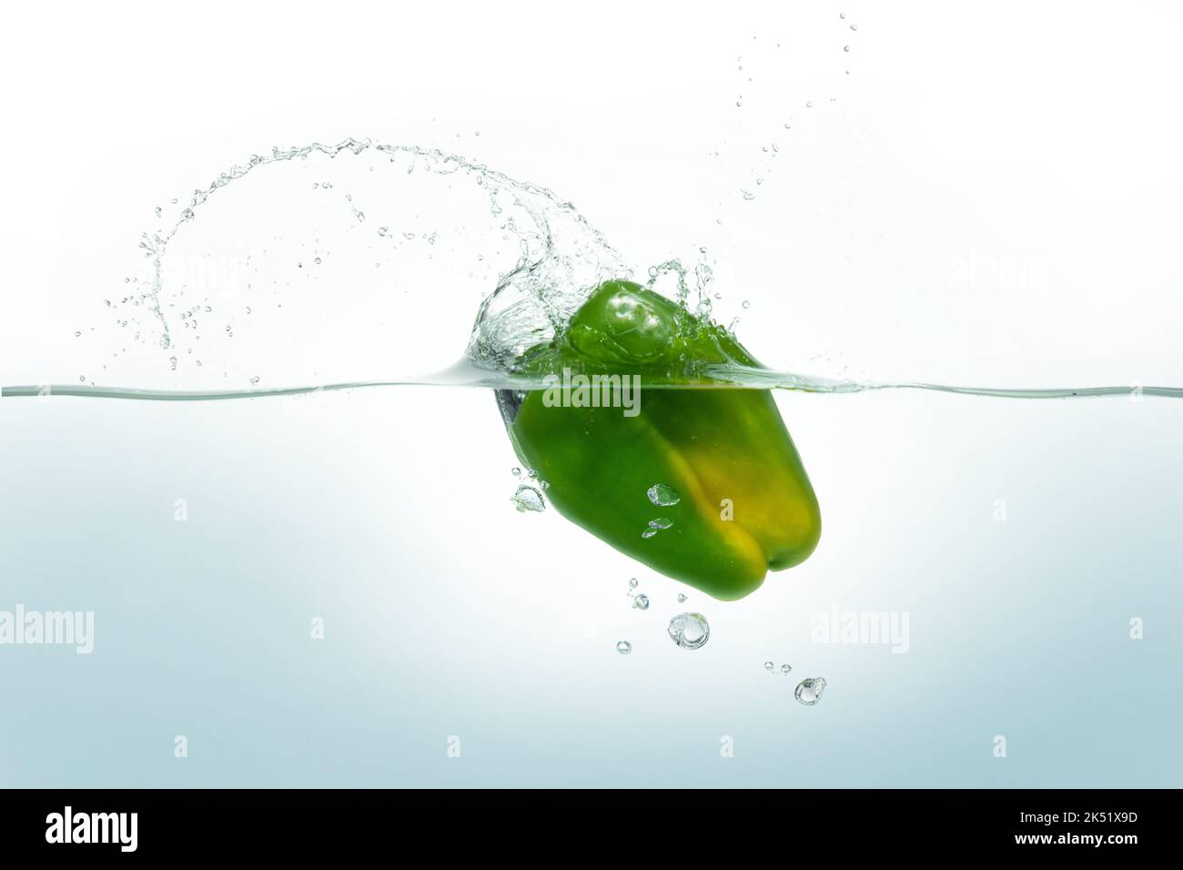 Grüner Pfeffer, der in Wasser spritzt. Seitenansicht auf weißem Hintergrund. Stockfoto