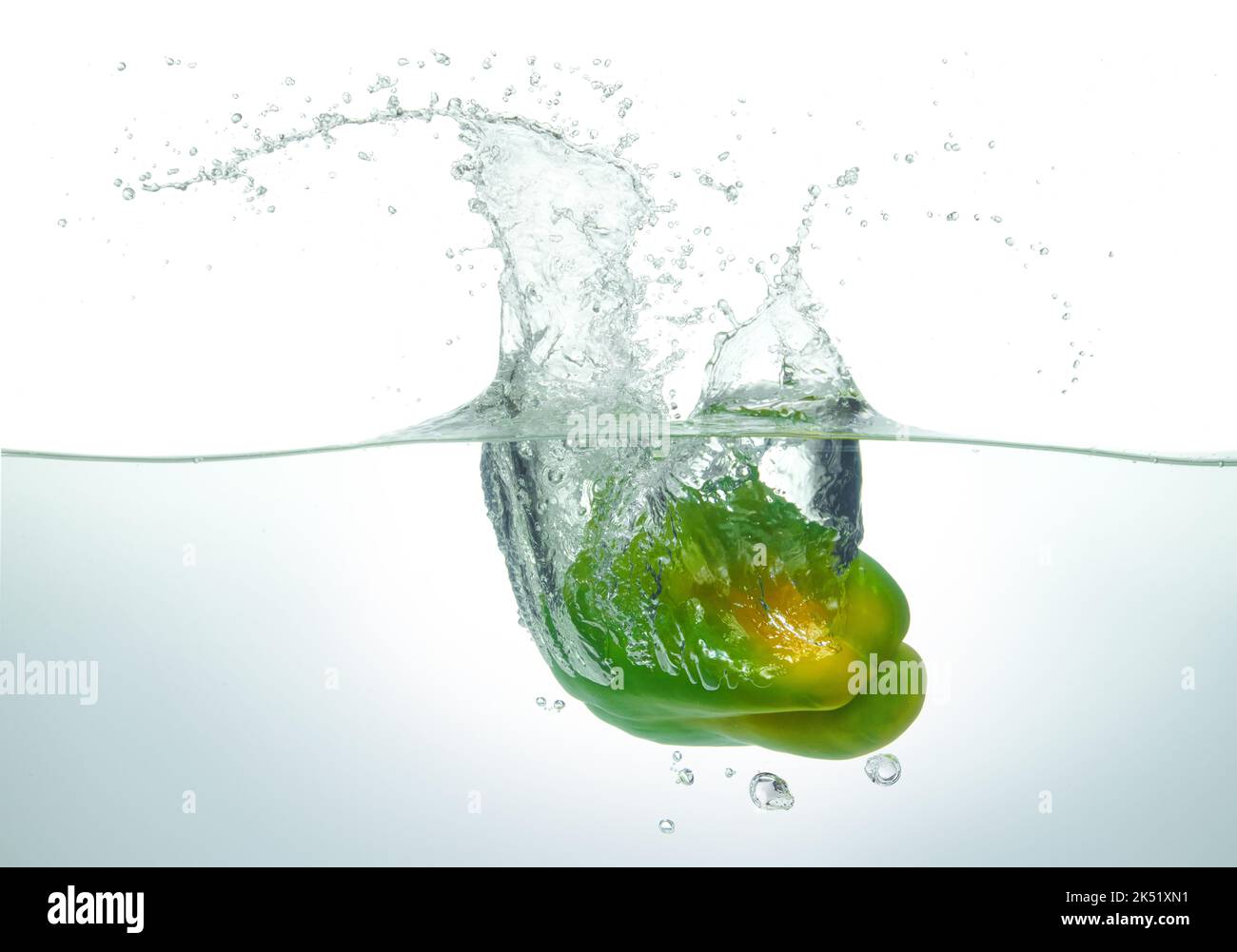 Grüner Pfeffer, der in Wasser spritzt. Seitenansicht auf weißem Hintergrund. Stockfoto