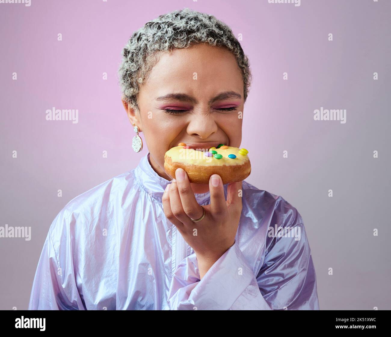 Essen, Studio und Frau essen einen Donut-Kuchen mit geschlossenen Augen und genießen süßes Sahnehäubchen und Zuckergebäck allein. Hungrige junge Mädchen auf eine Fast-Food-Diät mit Stockfoto