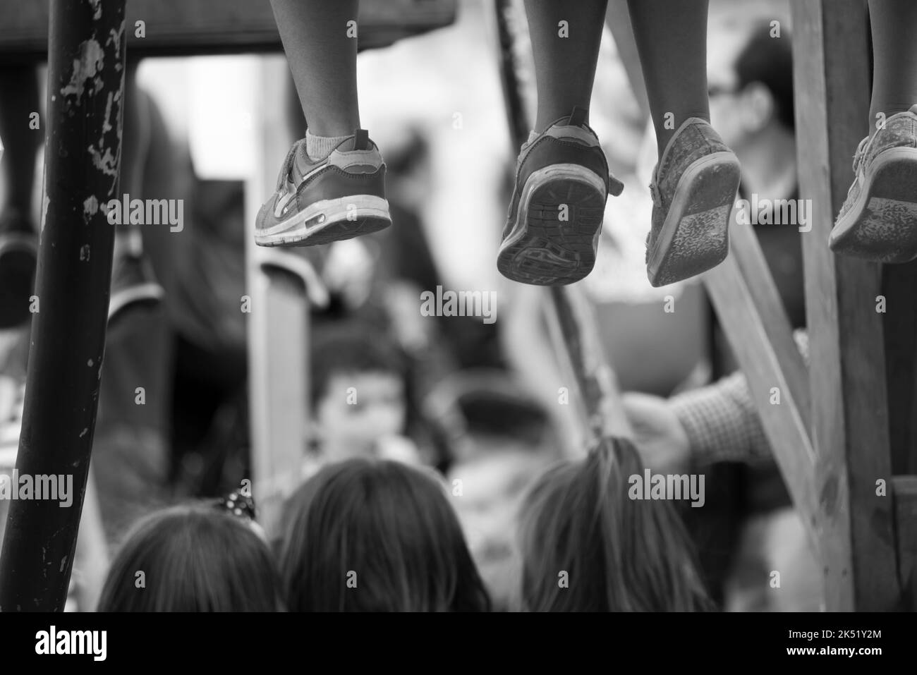 Eine Gruppe von Kindern, die sich eine Straßenshow ansehen, sieht nur, wie ihre Füße auf den Ständer schlagen und ihre Köpfe auf dem Rücken, aufgenommen in Schwarzweiß Stockfoto