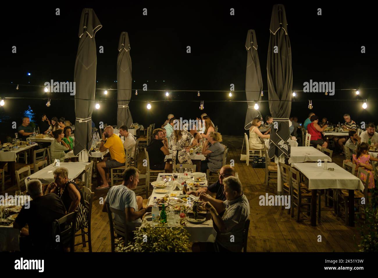 Nea Kallikrateia, Griechenland - 28. August 2022 : Griechen und Touristen genießen das Abendessen im Freien in einem gemütlichen beleuchteten Restaurant vor dem Meer Stockfoto