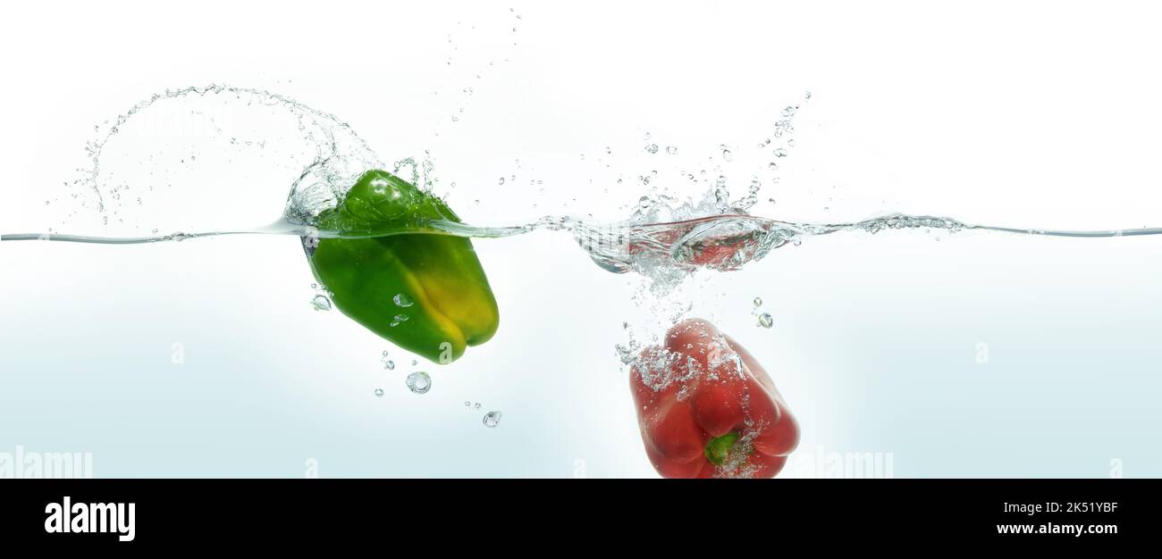 Zwei Paprika grün und rot spritzt in Wasser. Seitenansicht auf weißem Hintergrund. Stockfoto