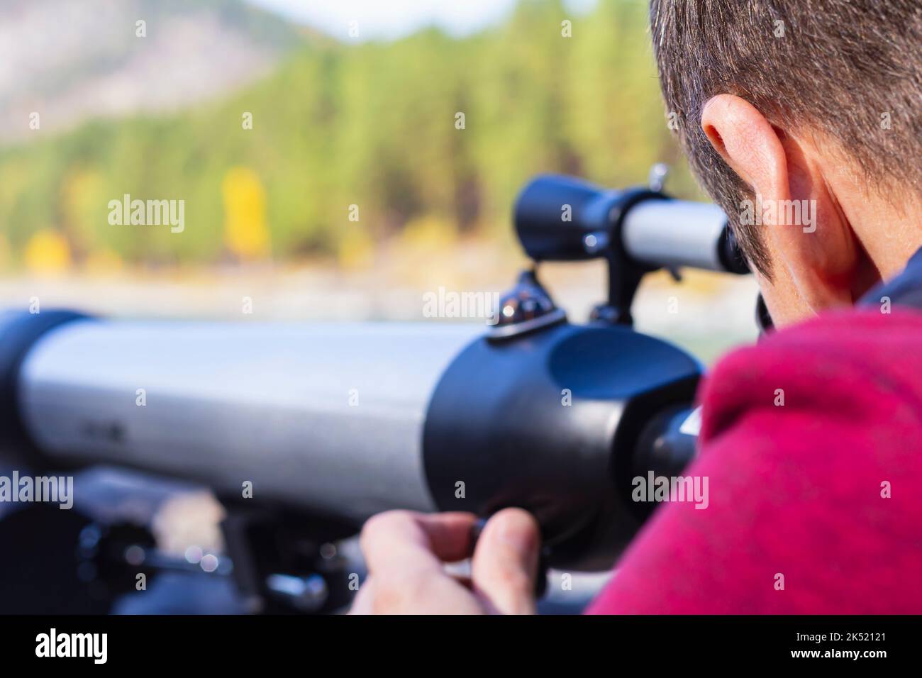 Fokussiere dich auf den Kopf des Menschen und schaue auf Berggipfel im Teleskop im Tal des Gebirgsflusses, selektiver Fokus. Optisches Teleskop, außer Fokus, Geräteinstr Stockfoto