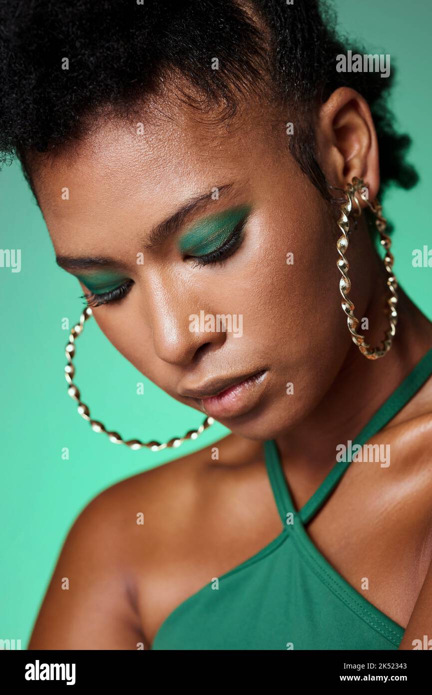 Schönheit, grüne Mode und Make-up mit einer schwarzen Frau im Studio auf einem Wandhintergrund mit Lidschatten und Schmuck. Gesicht, Kosmetik und Accessoires mit Stockfoto