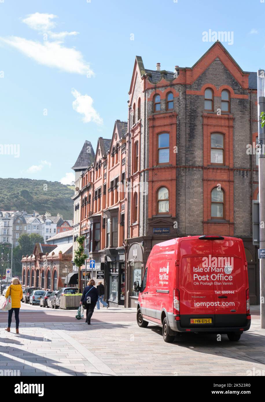 Ein charakteristisches rotes Postauto im Stadtzentrum von Douglas, eine Menscheninsel mit viktorianischen Gebäuden und Passanten in der Ferne. Stockfoto Ein charakteristisches rotes Postauto im Stadtzentrum von Douglas, eine Menscheninsel mit viktorianischen Gebäuden und Passanten in der Ferne. Stockfoto