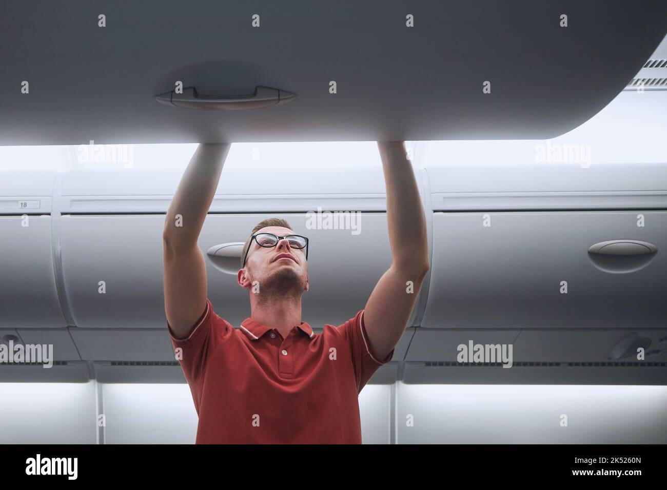 Mann reist mit dem Flugzeug. Passagier, der Handgepäck in Schließfächern über den Sitzen des Flugzeugs verstaut. Stockfoto