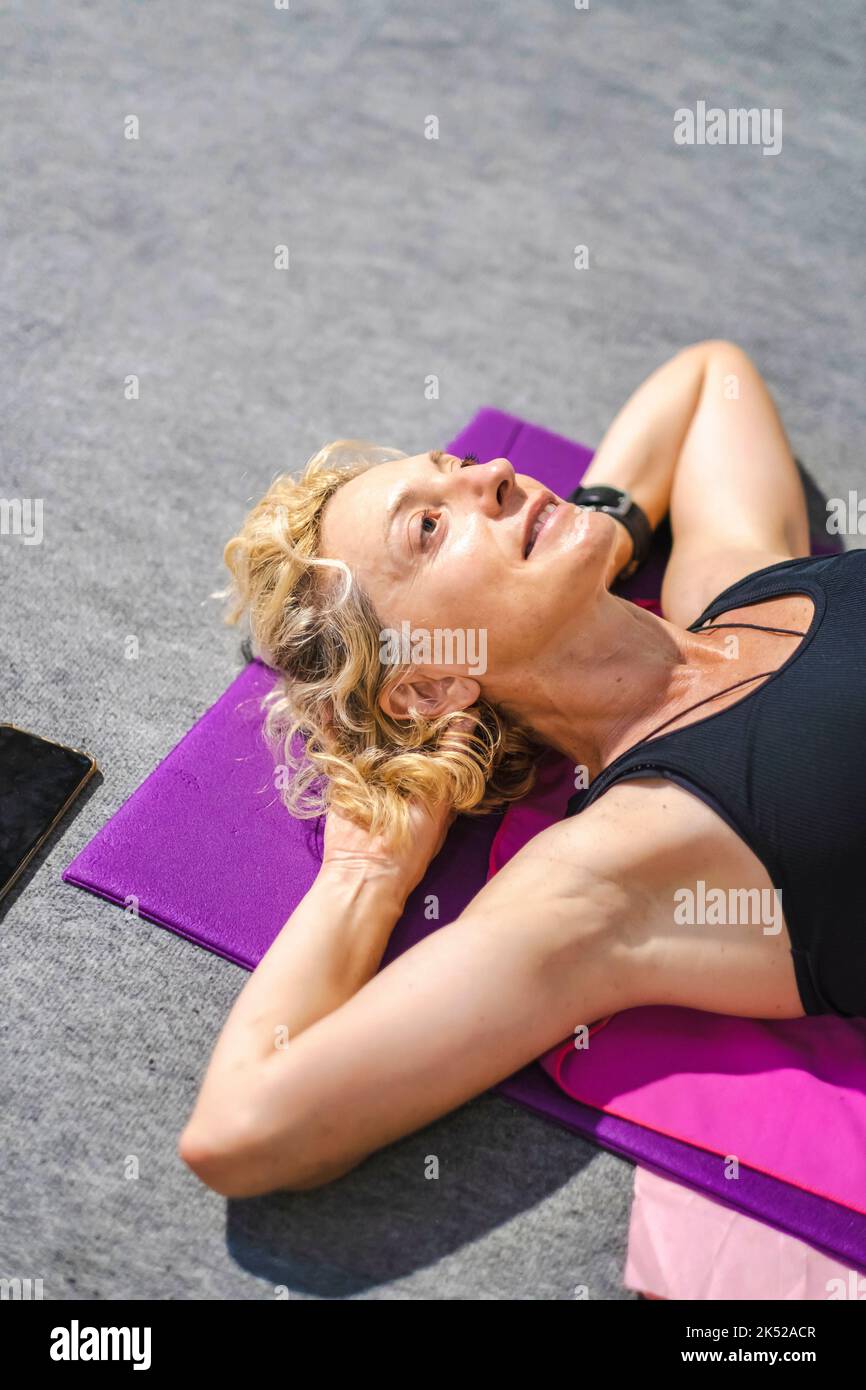 Echte junge reife kaukasische Frau in einer Sportkleidung in einem Fitnessstudio mit einem Mobiltelefon tun knirscht auf einer Matte. Fitnesskonzept. Stockfoto