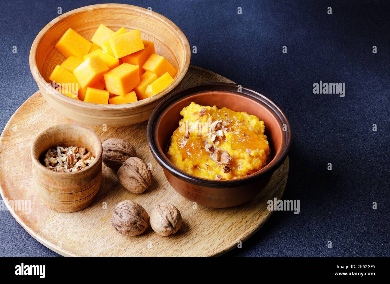 Süßer Kürbisbrei in Tonschüssel mit Marmelade und Nüssen und rohen Kürbiswürfeln Stockfoto