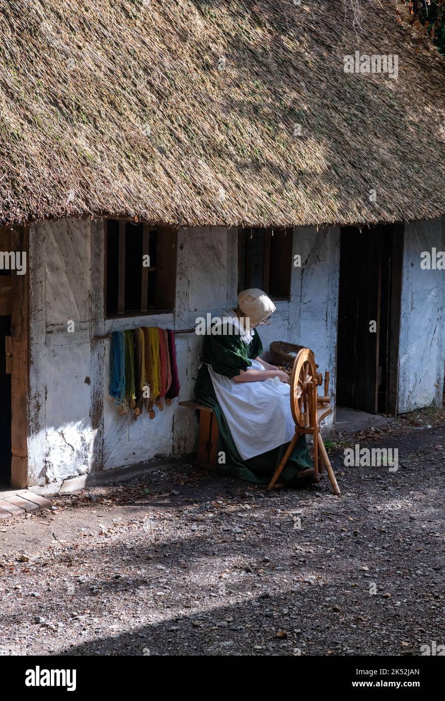 Frau in traditioneller Tracht, die Baumwolle auf einem traditionellen Spinnrad spinnt, kleines mittelalterliches Erholungsdorf in Woodham, in der Nähe von Gosport, England. Stockfoto