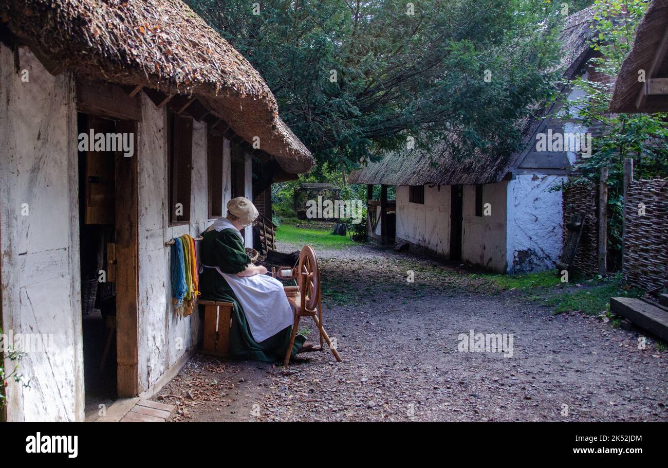 Frau in traditioneller Tracht, die Baumwolle auf einem traditionellen Spinnrad spinnt, kleines mittelalterliches Erholungsdorf in Woodham, in der Nähe von Gosport, England. Stockfoto