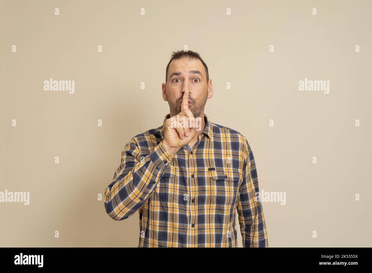 Ernst gut aussehende Männchen, hält den Vorderfinger auf den Lippen, versucht Verschwörung zu halten, schaut beiseite, sagt: Shh, bitte schweigt. Einzelaufnahme von Stockfoto