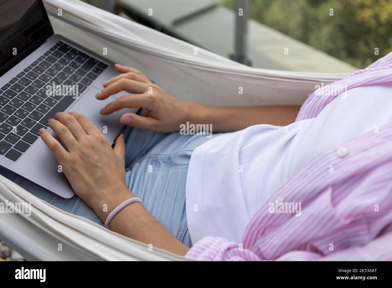 Junge freiberufliche Mitarbeiterin, die in Hängematte auf der Terrasse arbeitet Stockfoto