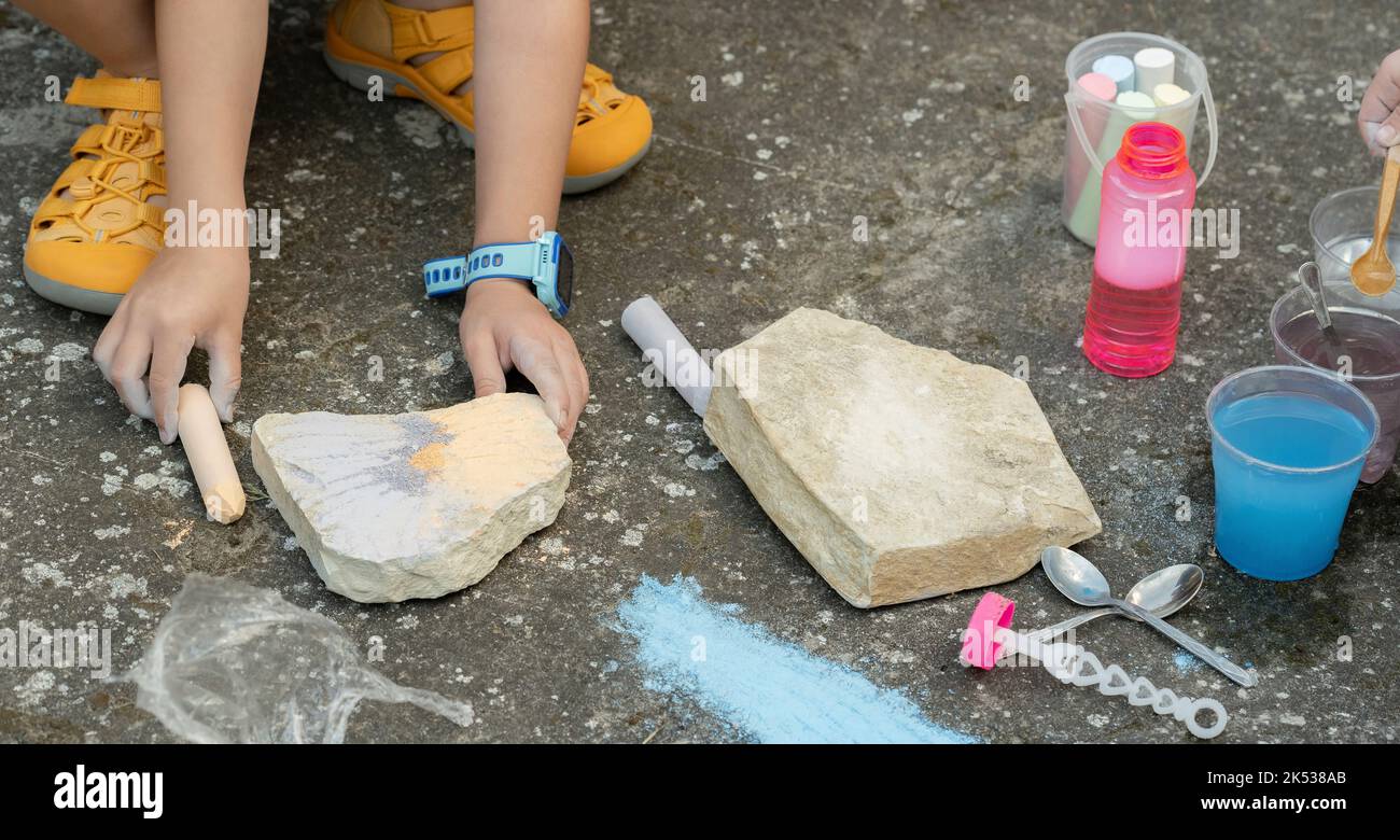 Anonymes Mädchen im Schulalter, das im Freien mit Kreide und Felsen spielt, Erholung im Freien, sensorische Integrationstherapie im Kindesalter. Nahaufnahme der Hände, Detailaufnahme Stockfoto
