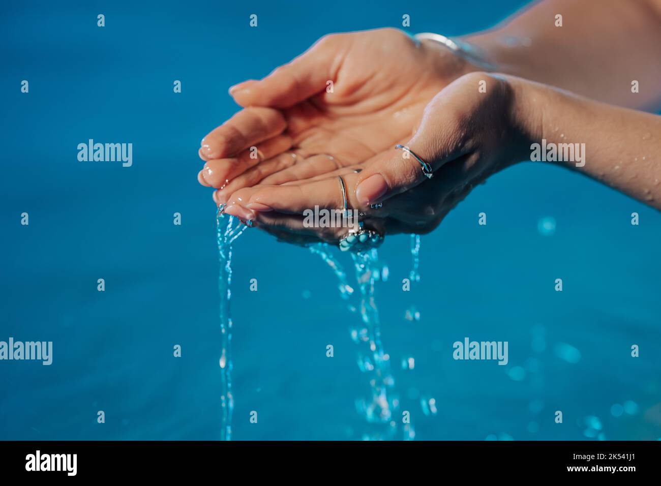 Sauberes Wasser in den Händen der Frau. Handflächen mit Zigeuner-Boho-Ringen mit klarem Aqua. Frische, Reinheit, lebensspendende Kraft, tropischer Hintergrund. Stockfoto