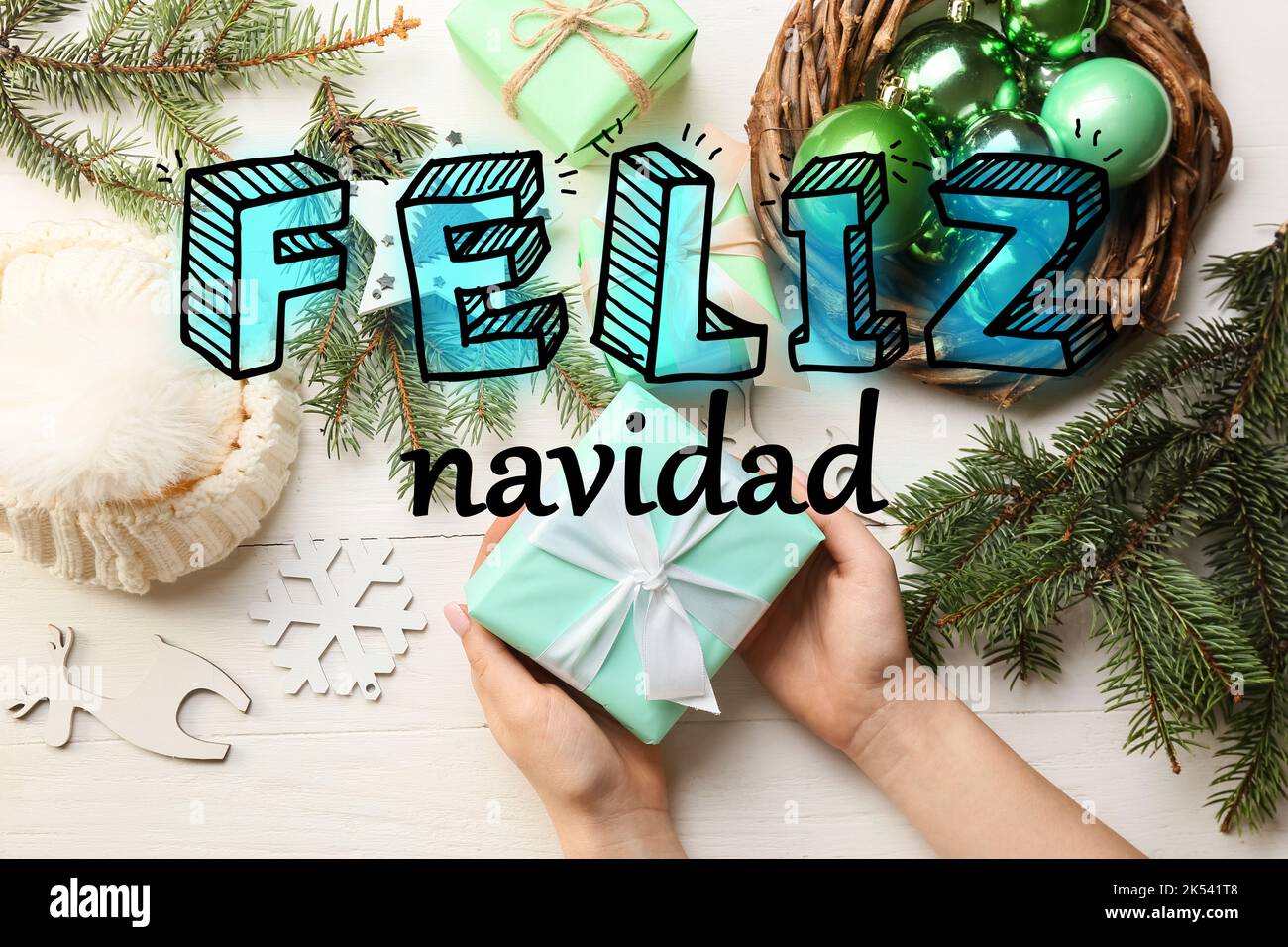 Weibliche Hände mit Geschenk, Dekor und Text FELIZ NAVIDAD (Spanisch für Frohe Weihnachten) auf hellem Hintergrund, Draufsicht Stockfoto