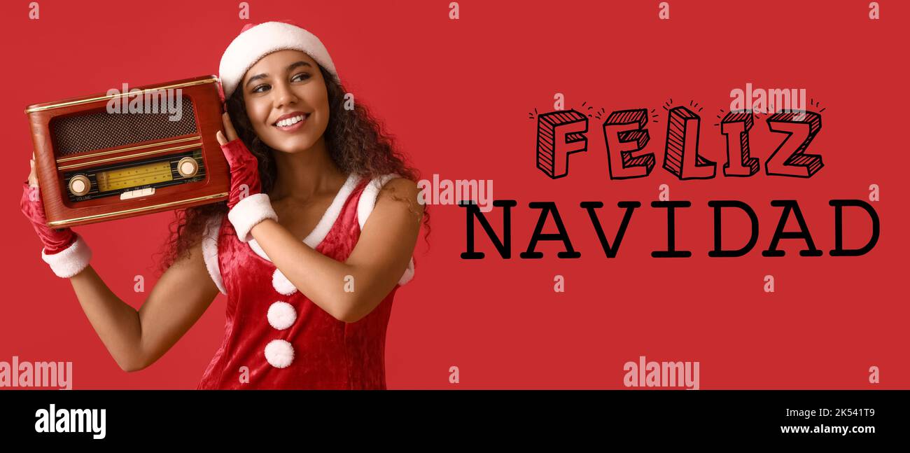 Junge afroamerikanische Frau im Weihnachtsmann-Hut mit Retro-Radioempfänger und Text FELIZ NAVIDAD (Spanisch für Frohe Weihnachten) auf rotem Hintergrund Stockfoto