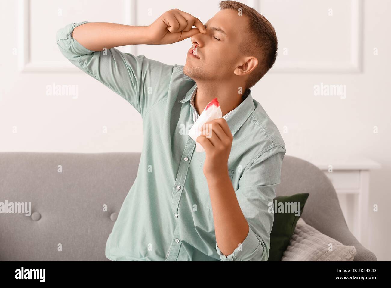 Junger Mann mit Nasenbluten und Gewebe zu Hause Stockfoto