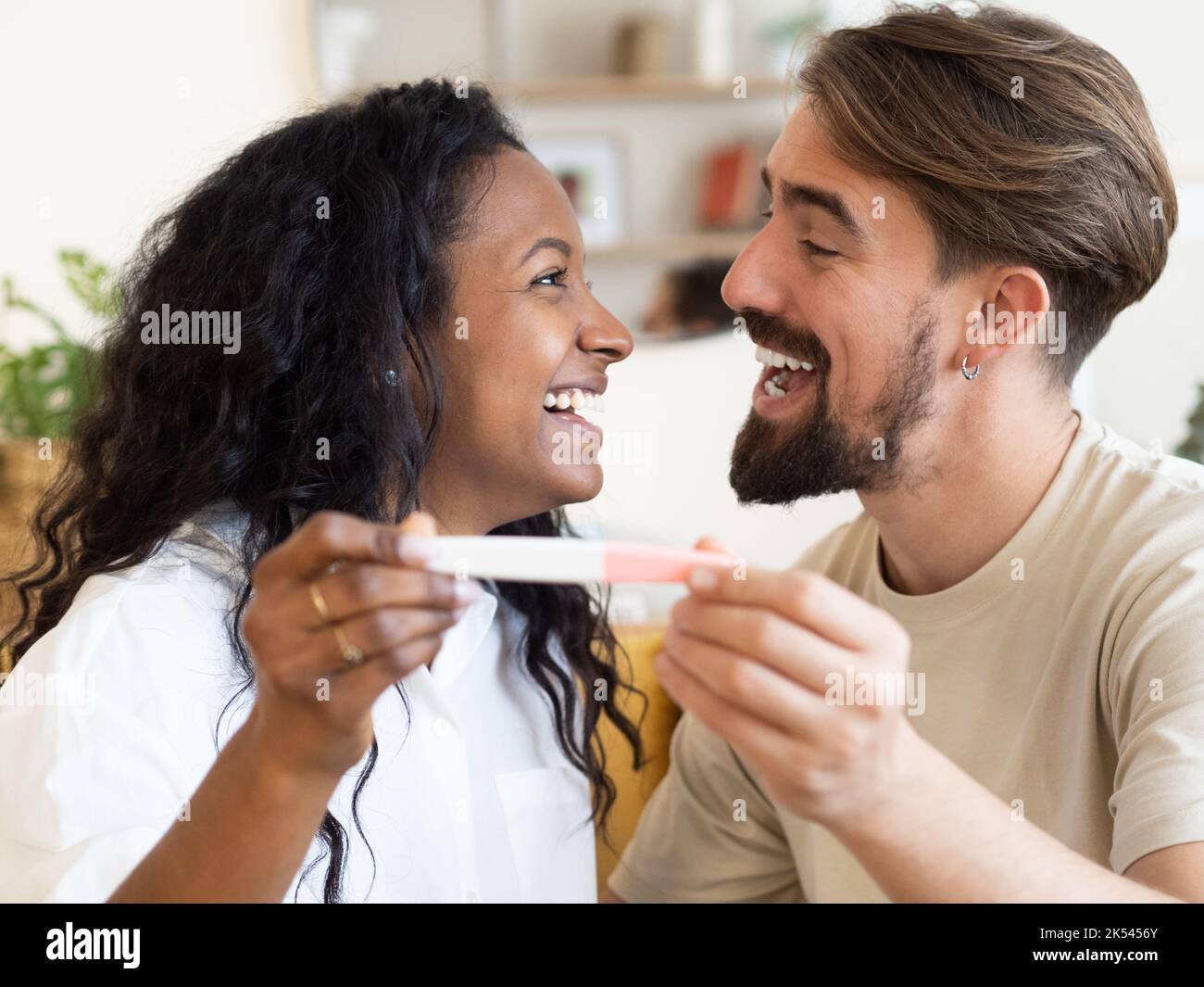 Ein junges multiethnisches Paar blickt glücklich auf einen Schwangerschaftstest. Schwangerschaft feiern Stockfoto