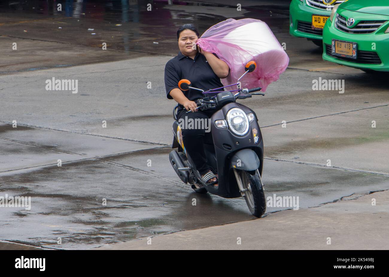 SAMUT PRAKAN, THAILAND, SEP 23 2022, Eine Frau fährt ein Motorrad und hält ein Telefon und eine große Tasche mit Ladung in einer Hand Stockfoto