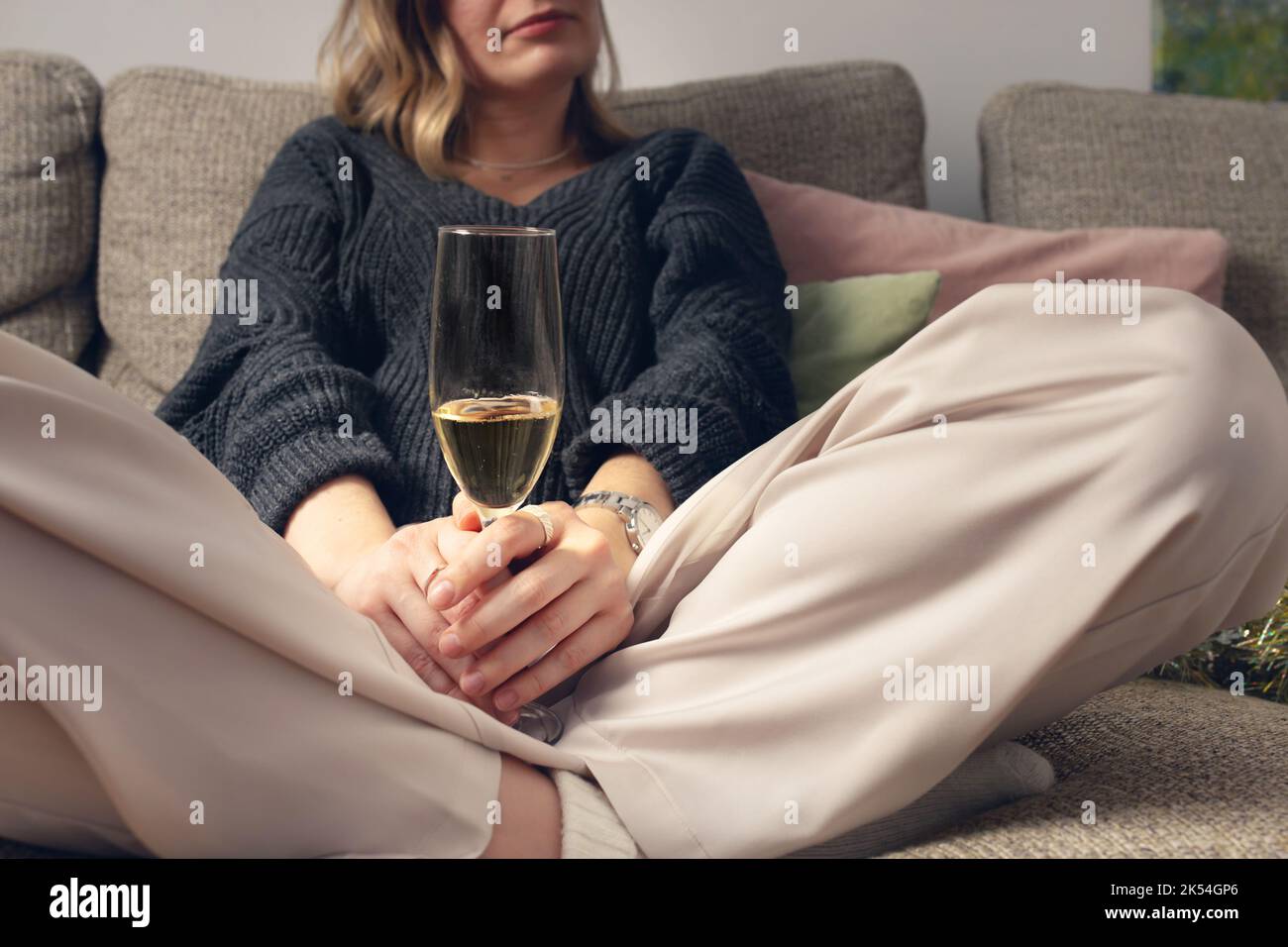 Eine Frau sitzt mit einem Glas Champagner in ihrem Schlafanzug auf der Couch. Vorderansicht. Stockfoto