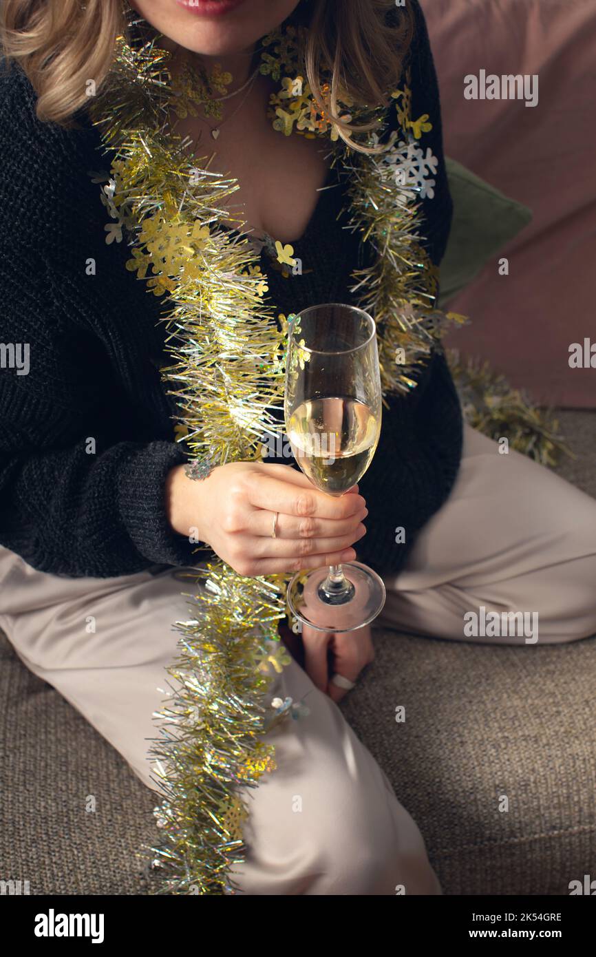 Eine Frau sitzt mit einem Glas Champagner in ihrem Schlafanzug auf der Couch. Vorderansicht. Stockfoto