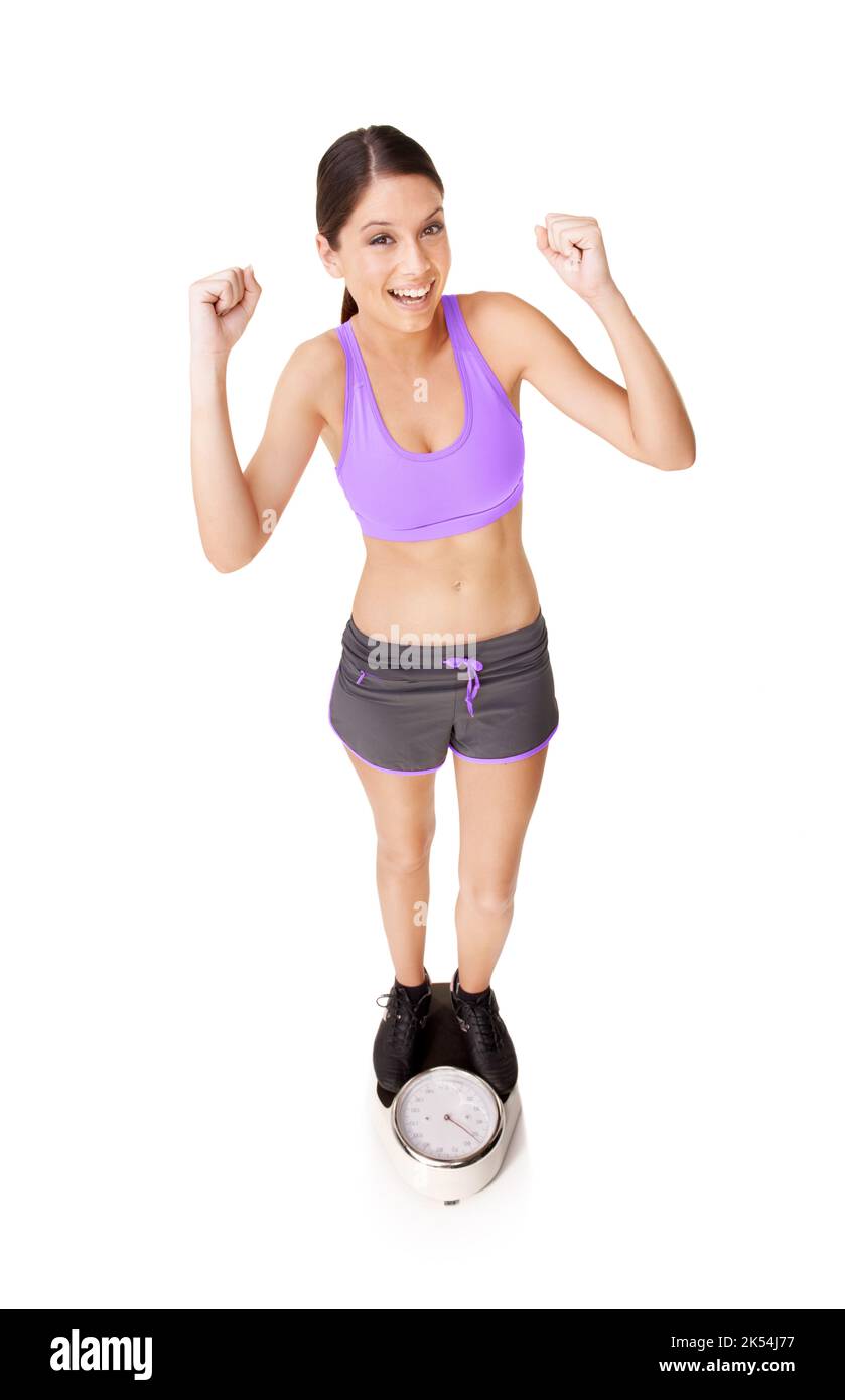 Ihr Ziel zu erreichen, ist eine Feier wert. In voller Länge, in einem hohen Winkel, eine ekstatische junge Frau, die sich auf einer weißen, isolierten Skala wägt. Stockfoto