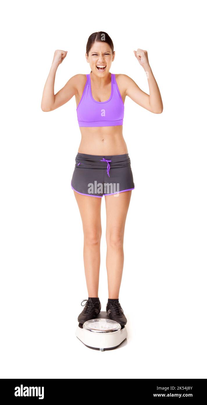 Wir feiern ihre Erfolge. Ganzkörperaufnahme einer ekstatischen jungen Frau, die sich auf einer isolierten Skala auf Weiß wägt. Stockfoto