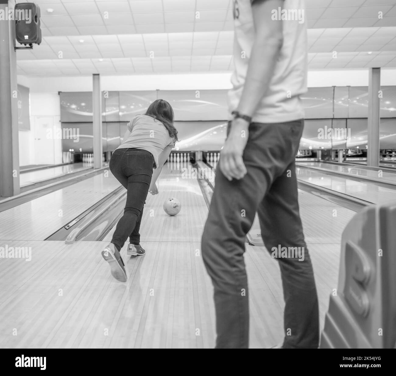 Eine Frau wirft einen Ball in eine Bowlingbahn. Wege mit Bällen und Pins zum Bowling. Ein lustiges Spiel für das Unternehmen. Stockfoto