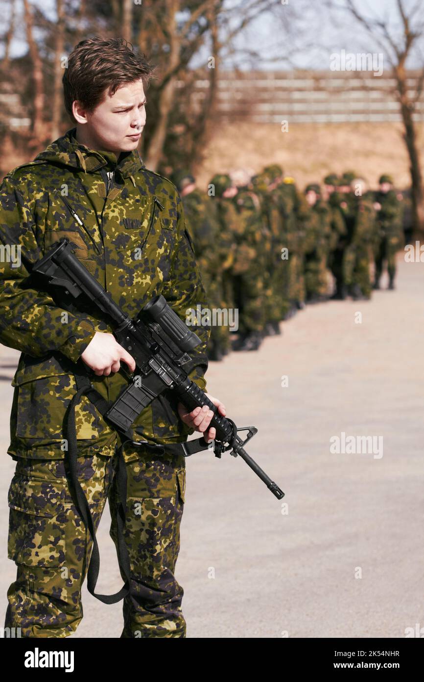 Hoch stehend. Ein Soldat, der mit einem Gewehr steht, und seine Mitsoldaten im Hintergrund. Stockfoto