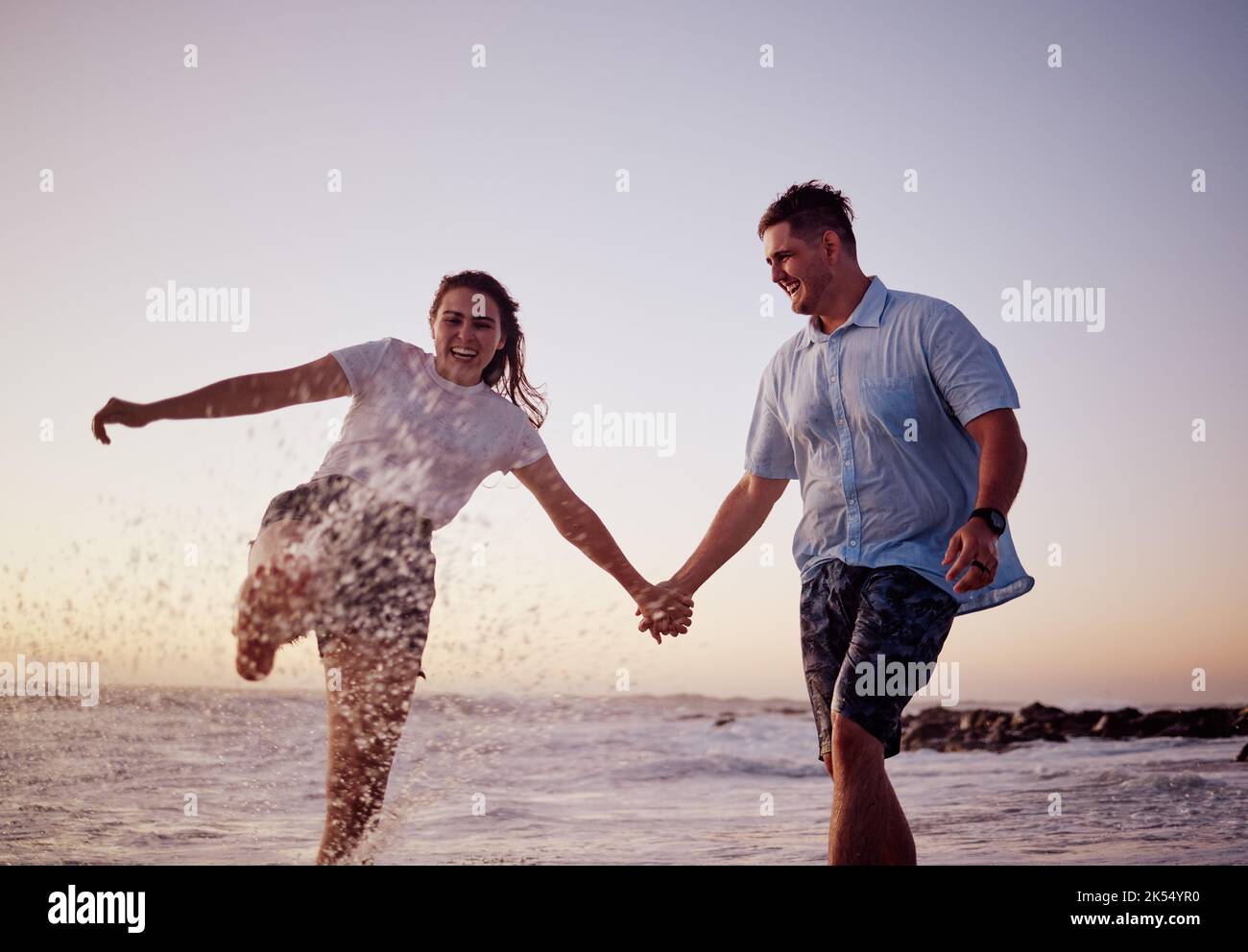 Strandwasser planschen, Paare und glückliche Menschen zusammen fühlen Liebe und Spaß im Sommer bei Sonnenuntergang. Freundin und Freund halten die Hände im Meer Stockfoto