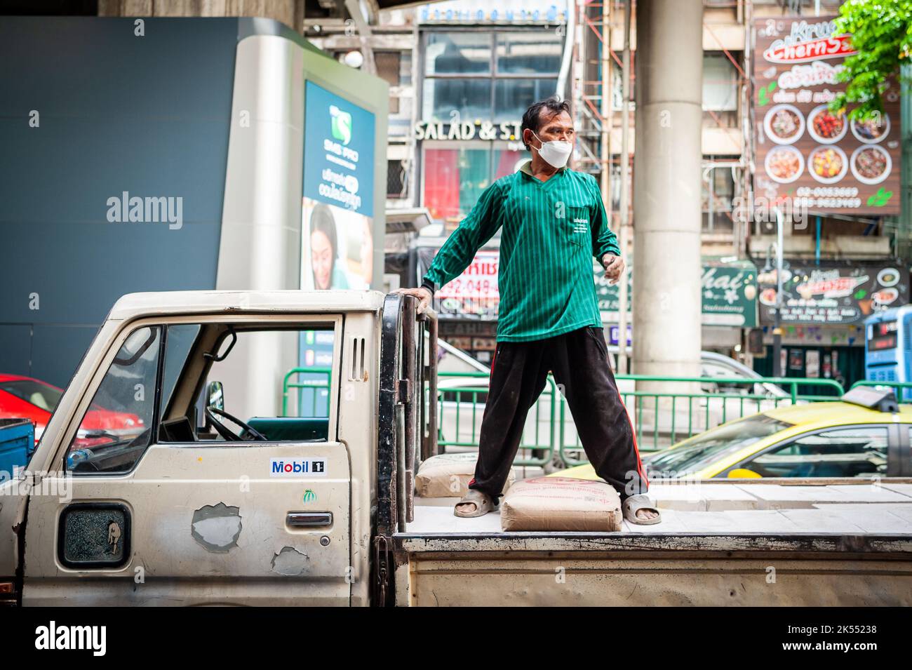 Thailändische Bauarbeiter entladen Zement oder Kies von der Rückseite eines Lastwagens auf der Silom Rd. Bangkok Thailand. Stockfoto