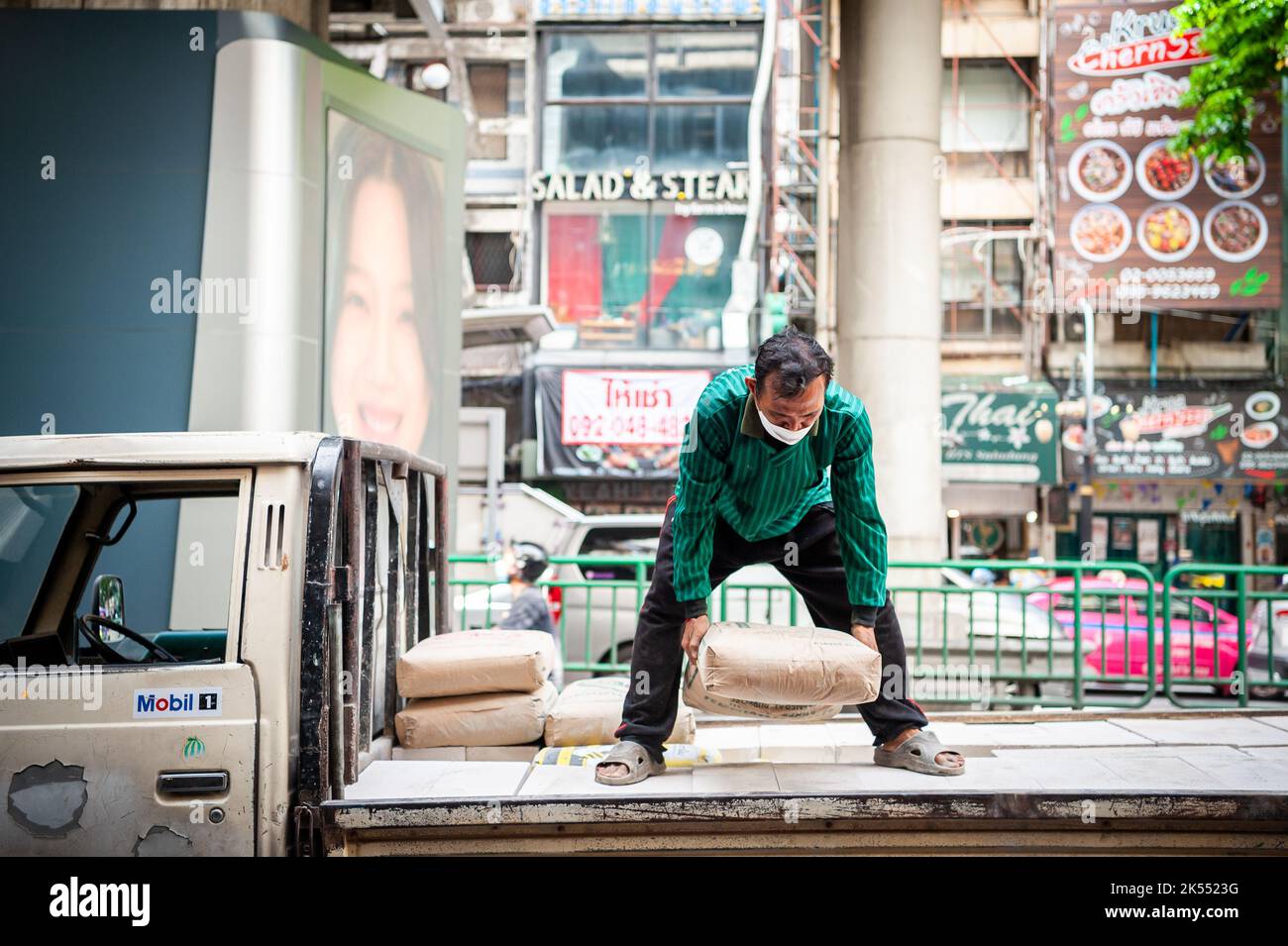 Thailändische Bauarbeiter entladen Zement oder Kies von der Rückseite eines Lastwagens auf der Silom Rd. Bangkok Thailand. Stockfoto