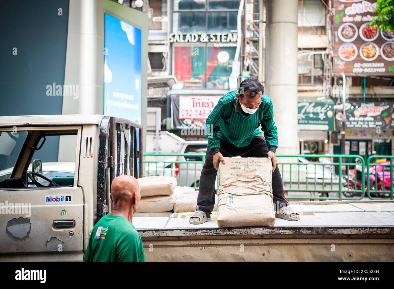 Thailändische Bauarbeiter entladen Zement oder Kies von der Rückseite eines Lastwagens auf der Silom Rd. Bangkok Thailand. Stockfoto