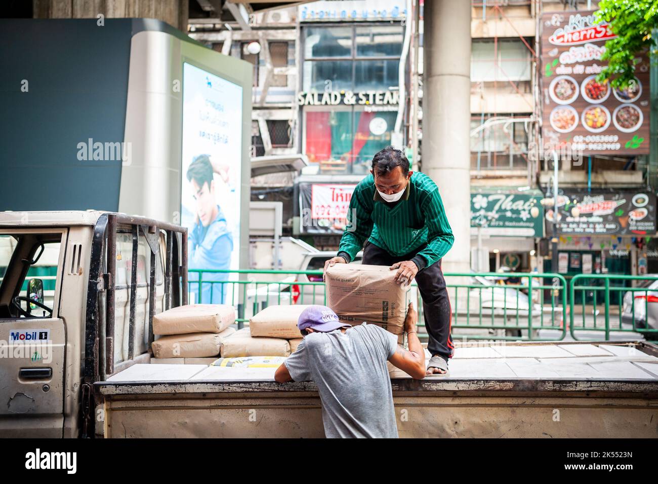 Thailändische Bauarbeiter entladen Zement oder Kies von der Rückseite eines Lastwagens auf der Silom Rd. Bangkok Thailand. Stockfoto