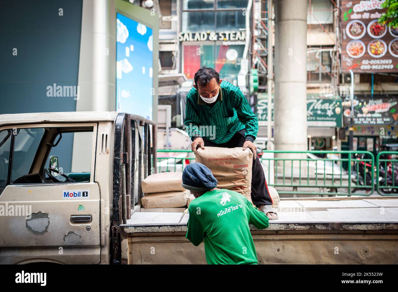Thailändische Bauarbeiter entladen Zement oder Kies von der Rückseite eines Lastwagens auf der Silom Rd. Bangkok Thailand. Stockfoto