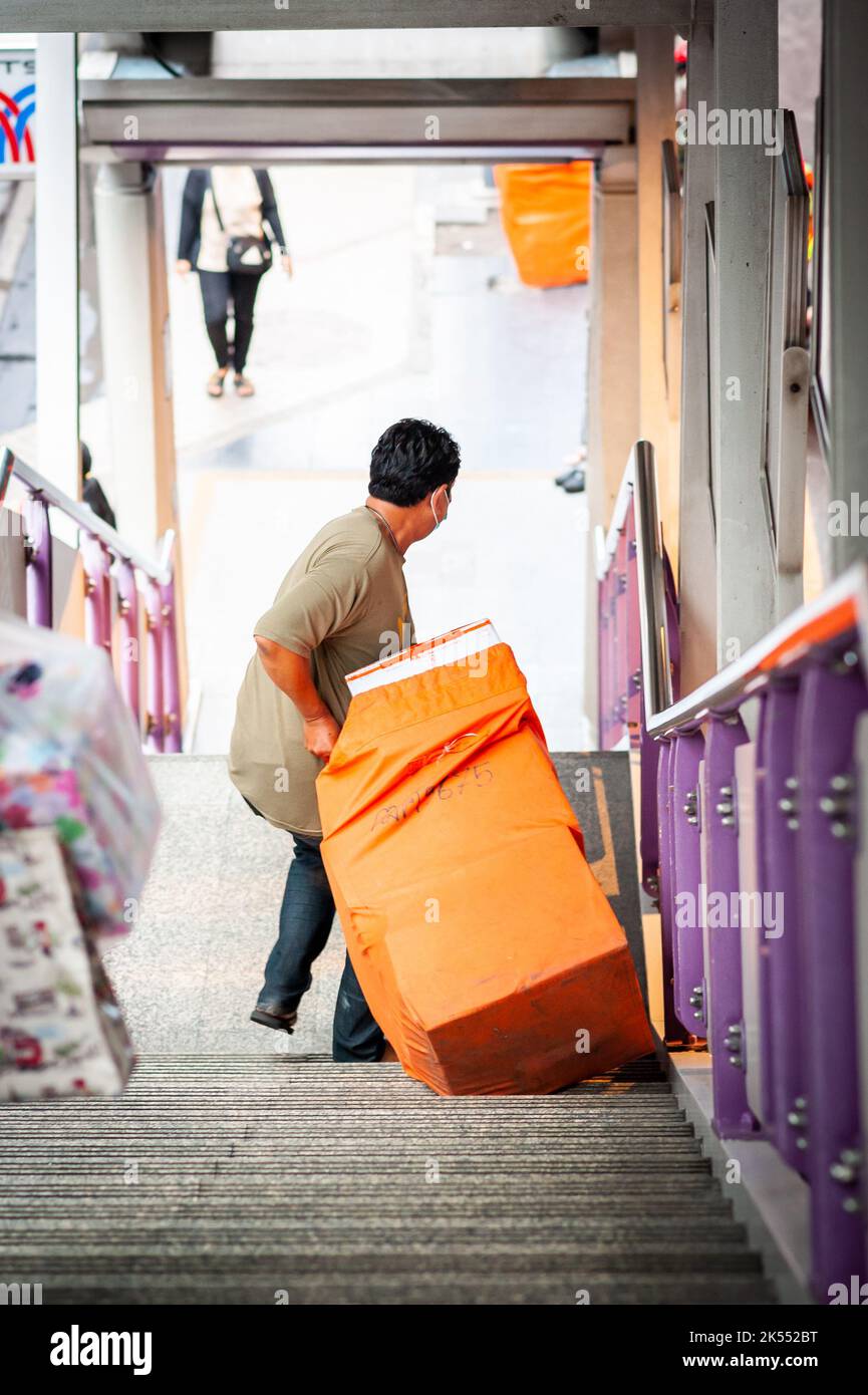 Ein Thailänder schleppt einen Postsack die Treppen des Skytrain-Bahnhofs Sala Daeng BTS in Bangkok Thailand hinunter. Stockfoto