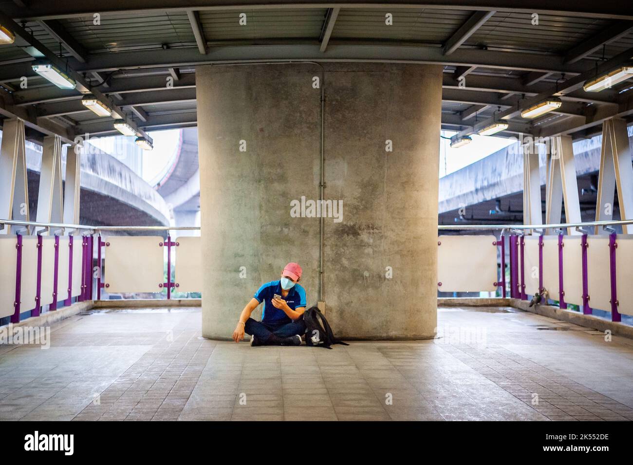 Ein einsamer junger Thailänder überprüft sein Handy auf dem Fußweg oder dem Skywalk über den geschäftigen Straßen von Bangkok, Thailand. Stockfoto