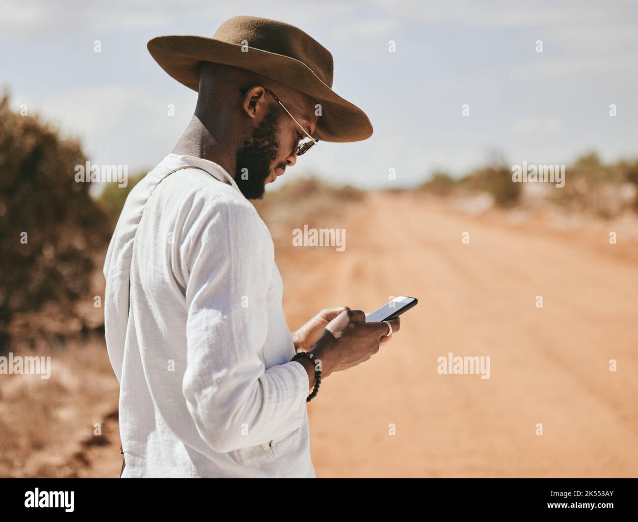 Dessert Feldweg, schwarzer Mann und Telefon Text in der Natur auf einen Urlaub verloren und warten auf einen Aufzug. 5G Internet-, Mobil- und Web-App-Nutzung einer Person Stockfoto