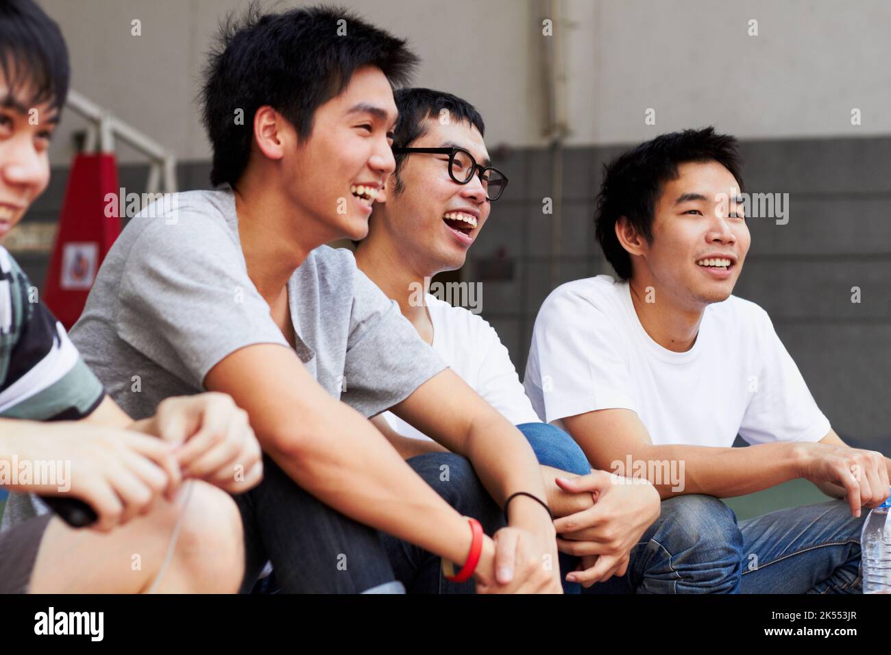 Typ, das ist super. Eine Gruppe asiatischer Jugendlicher, die zusammen lachen, während sie im Freien sitzen. Stockfoto