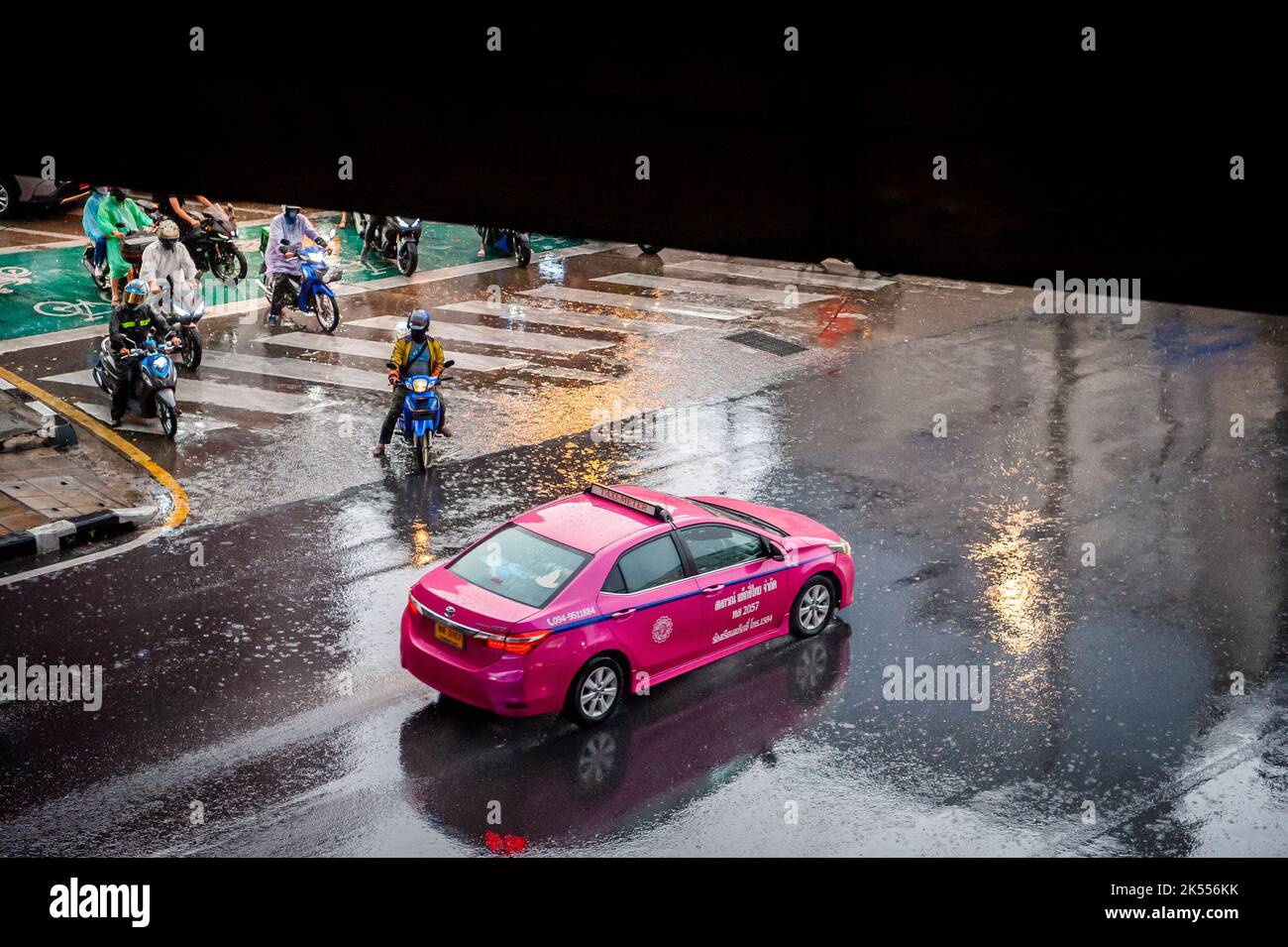 Autos, Minibusse, Busse und Motorräder passieren alle eine belebte Kreuzung an einem regnerischen, dunklen Tag zur Hauptverkehrszeit in Bangkok, Thailand. Stockfoto