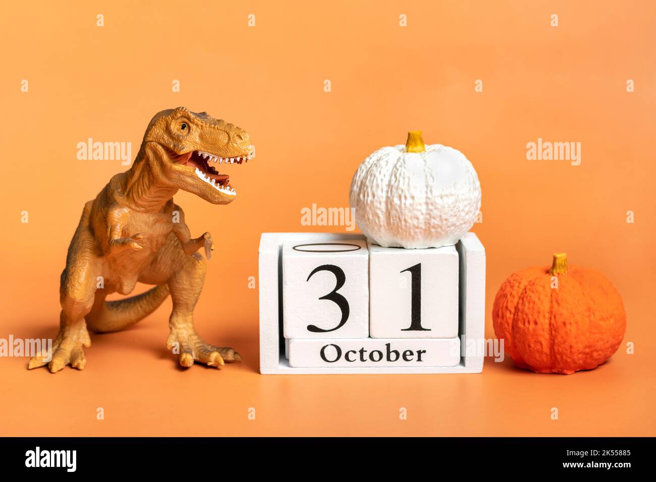 Spielzeug-Dinosaurier Tyrannosaurus Kürbis, Kalenderdatum 31 Oktober isoliert auf orangefarbenem Hintergrund Feiertag Grußkarte Glücklicher Halloween-Tag kreatives Minimalkonzept. Stockfoto